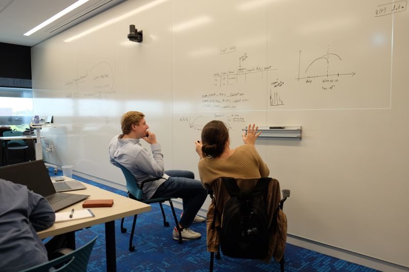 Two students work through disease-transmission models at a whiteboard covered in equations and epidemic curves.